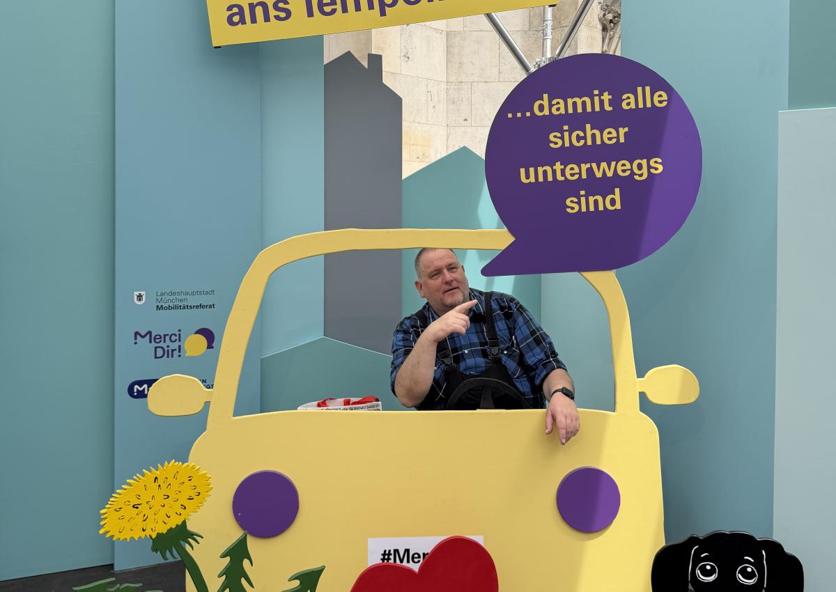 Ein Mann sitzt im Pop-up-Fotostudio von Merci Dir in einem Holzauto. Sein Statement: "Ich halte mich ans Tempolimit – damit alle sicher unterwegs sind"