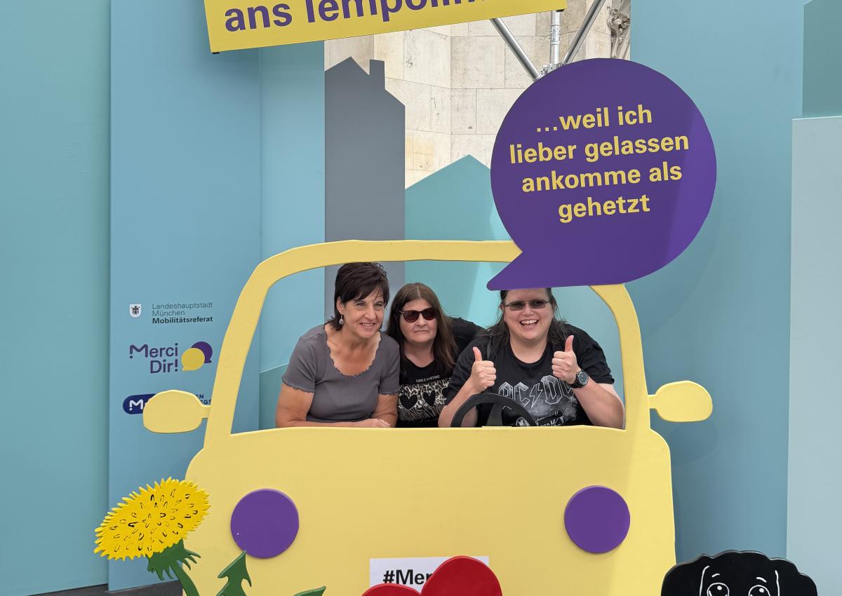 Drei Frauen sitzen im Pop-up-Fotostudio von Merci Dir in einem Holzauto. Ihr Statement: "Ich halte mich ans Tempolimit – weil ich lieber gelassen ankommen, als gehetzt"