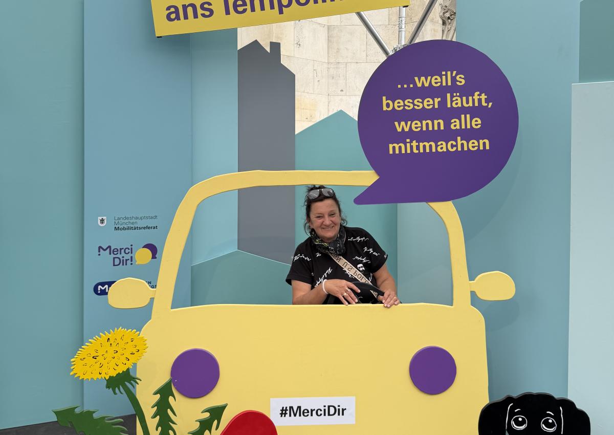 Eine Frau sitzt im Pop-up-Fotostudio von Merci Dir in einem Holzauto. Ihr Statement: "Ich halte mich ans Tempolimit – weil's besser läuft, wenn alle mitmachen"