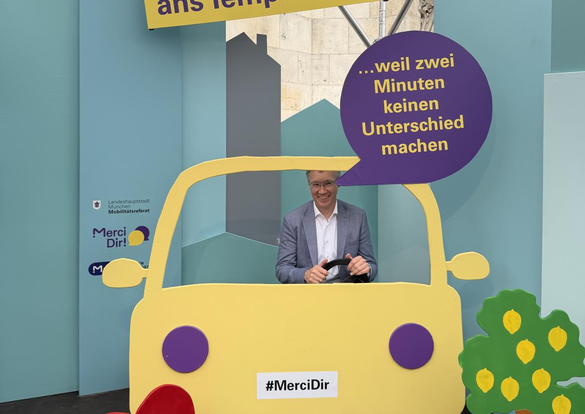 Mobilitätsreferent Georg Dunkel sitzt im Pop-up-Fotostudio von Merci Dir in einem Holzauto. Sein Statement: "Ich halte mich ans Tempolimit – weil zwei Minuten keinen Unterschied machen"